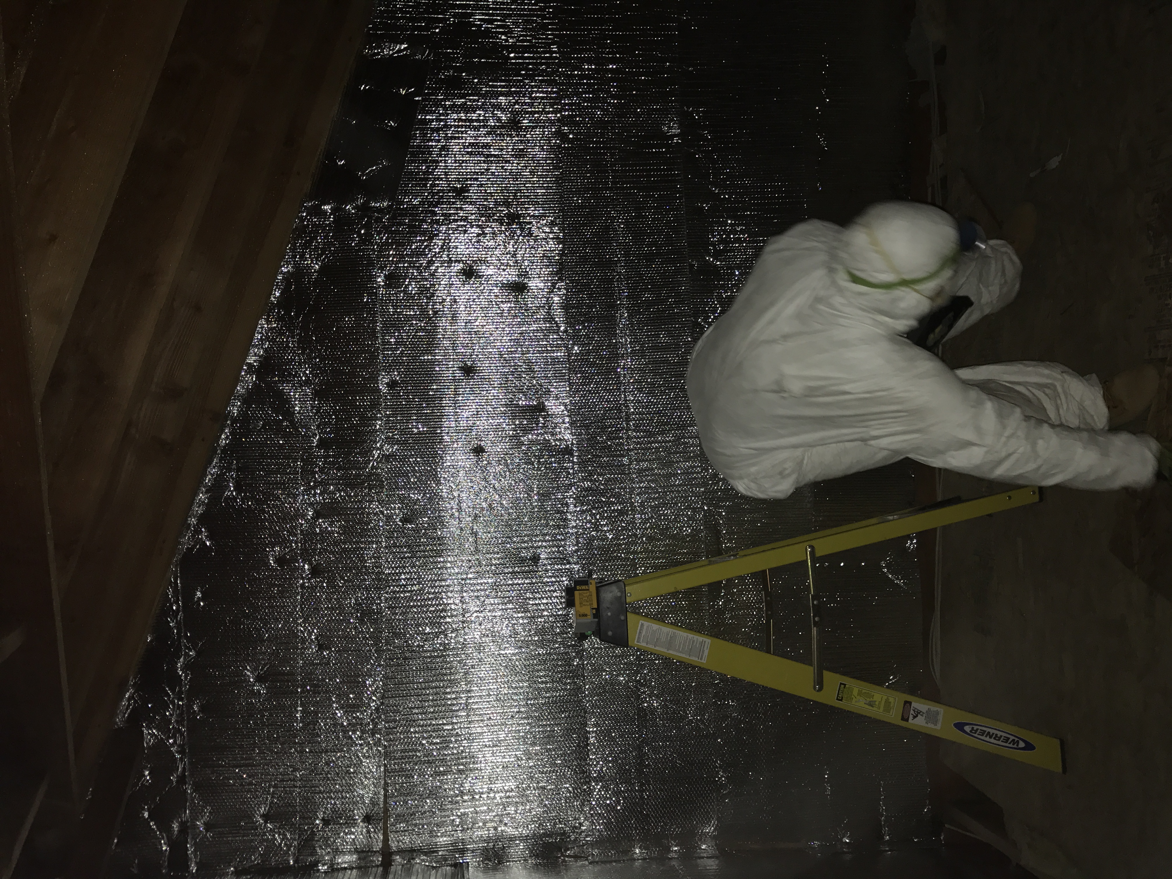 A Nu-Way crew member working in an attic with reflective wall covering.